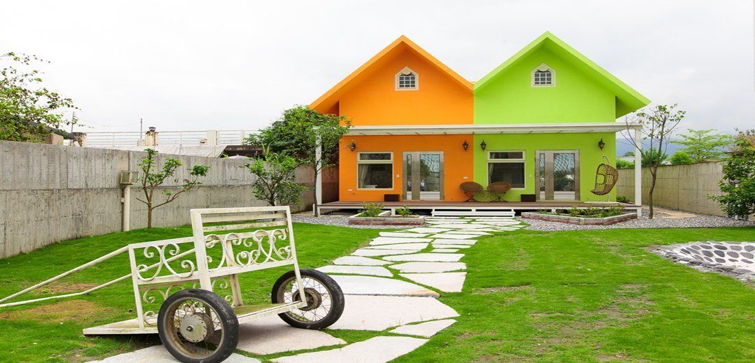 Une maison à deux étages avec une façade verte et orange, une allée pavée et un petit jardin.