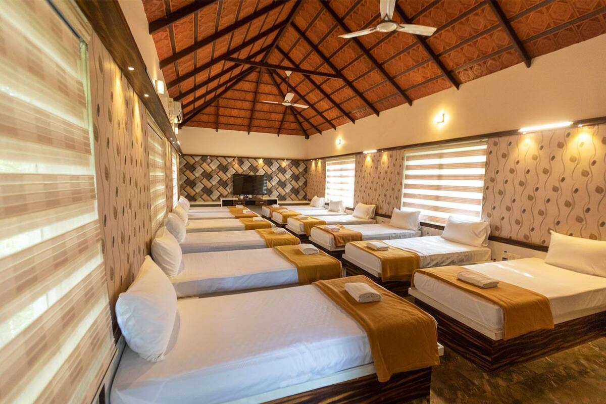 A hotel room with multiple beds arranged in a row, a ceiling fan, and a television on a stand.
