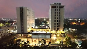 Un edificio moderno con techo plano y ventanas grandes, rodeado de construcciones más pequeñas y follaje.