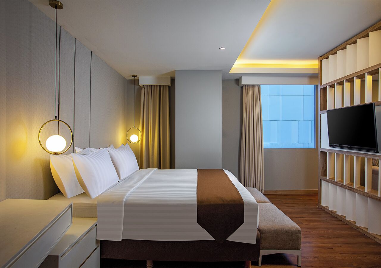 A hotel room with a bed, bedside table, TV, and a window with curtains.