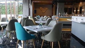 Un restaurante moderno con suelo de mármol, mesas y sillas ordenadas, y una obra de arte decorativa en la pared.