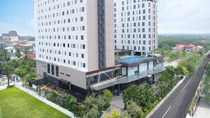 Un hotel moderno con varios pisos, una piscina en la azotea y un patio ajardinado.