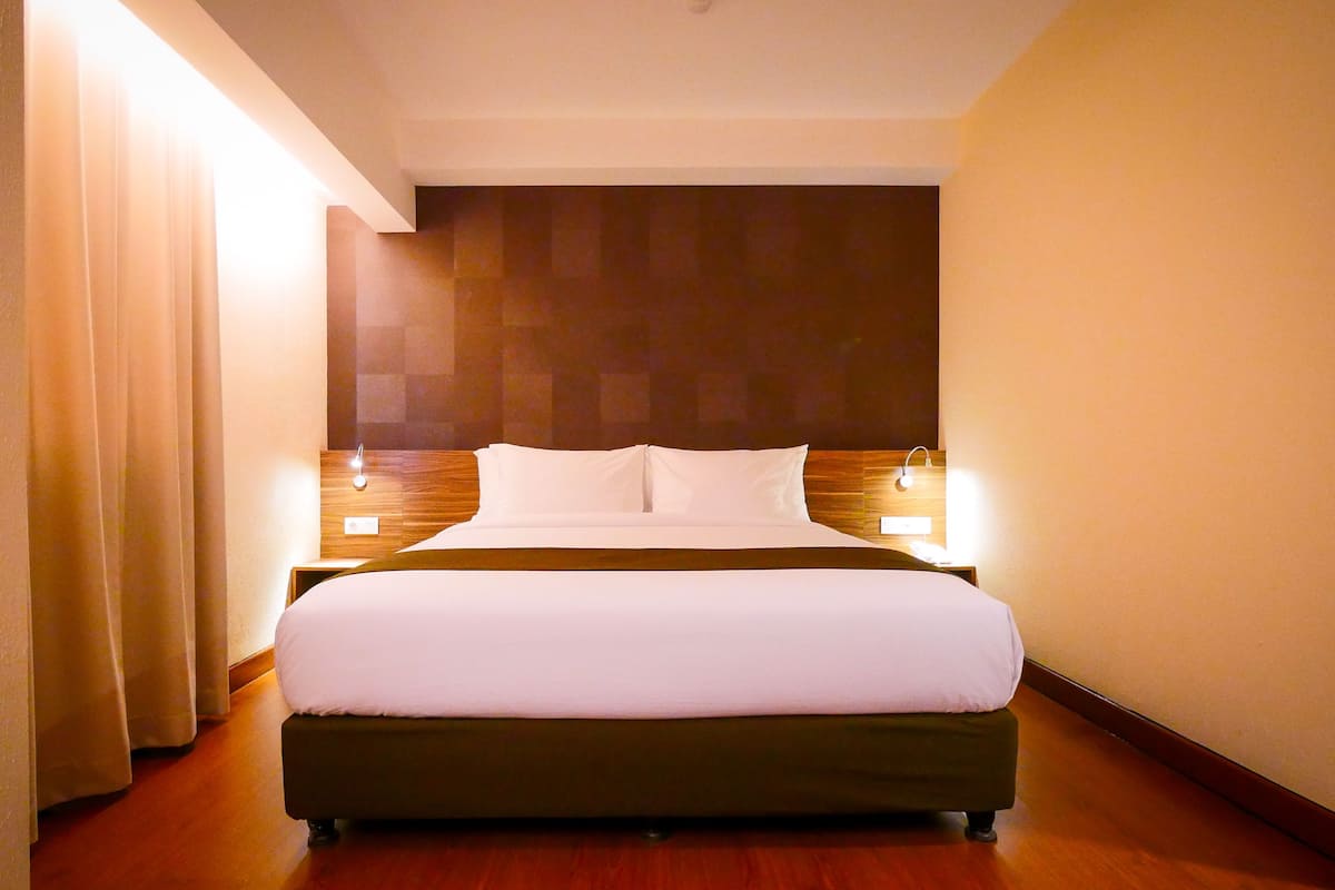Une chambre d’hôtel avec un grand lit, une tête de lit en bois, des lampes de chevet et un rideau sur le côté gauche.