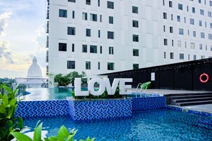 A modern hotel with a large pool area, a prominent 'LOVE' sign, and a dome-shaped building in the background.