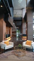 A modern lobby with a marble floor, two white armchairs with yellow cushions, a glass coffee table, and a decorative wall with geometric patterns.