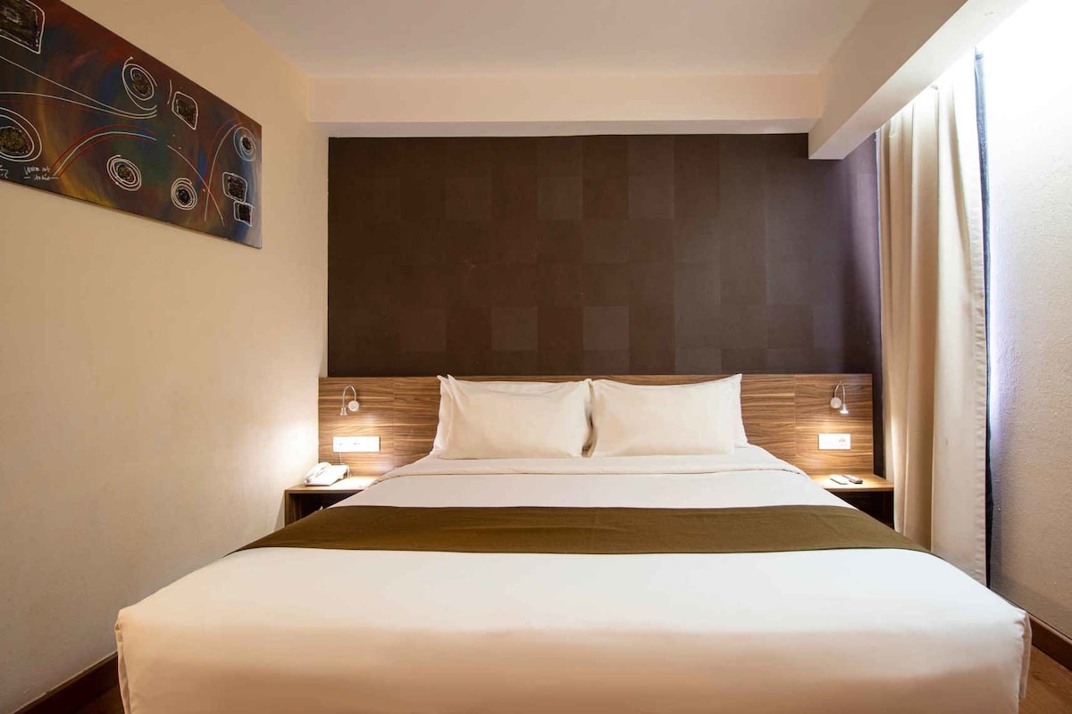 A hotel room with a large bed, two bedside tables, a headboard, and a painting on the wall.