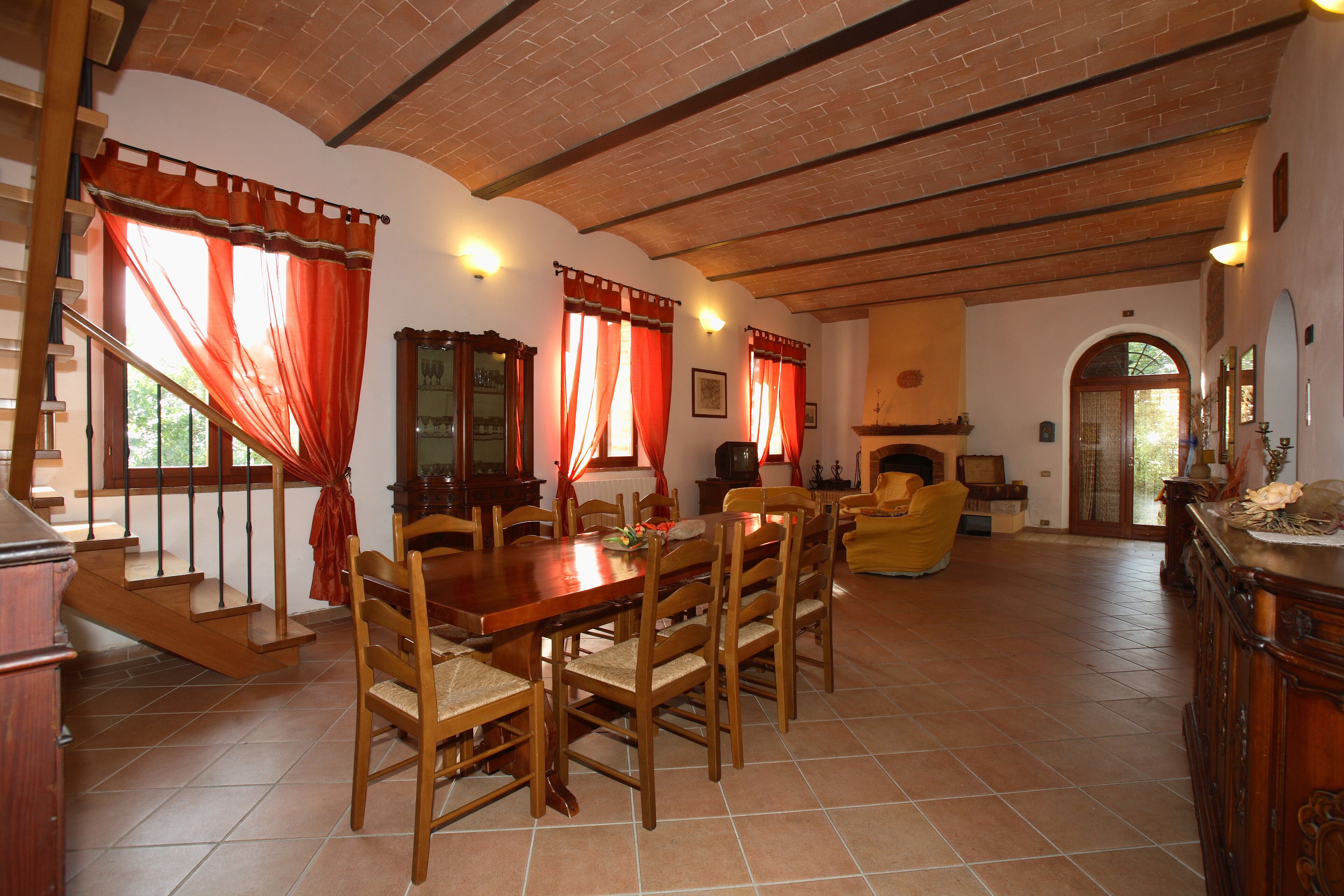 A spacious living room with a wooden dining table and chairs, a fireplace, and a staircase leading to an upper floor.