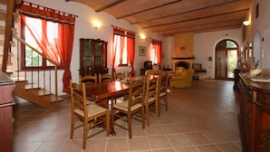 Un salón amplio con una mesa y sillas de madera, una chimenea y una escalera que sube a un nivel superior.
