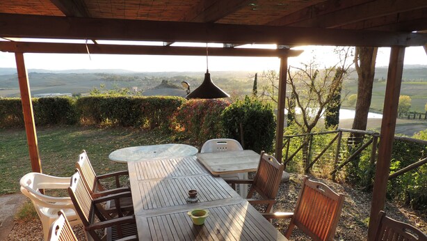 Un patio al aire libre con una mesa y sillas de madera, una lámpara colgante y vistas a un valle.