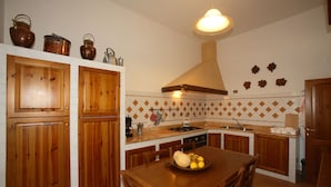 Una cocina con armarios de madera, una isla central con un bol de fruta y una lámpara colgante.