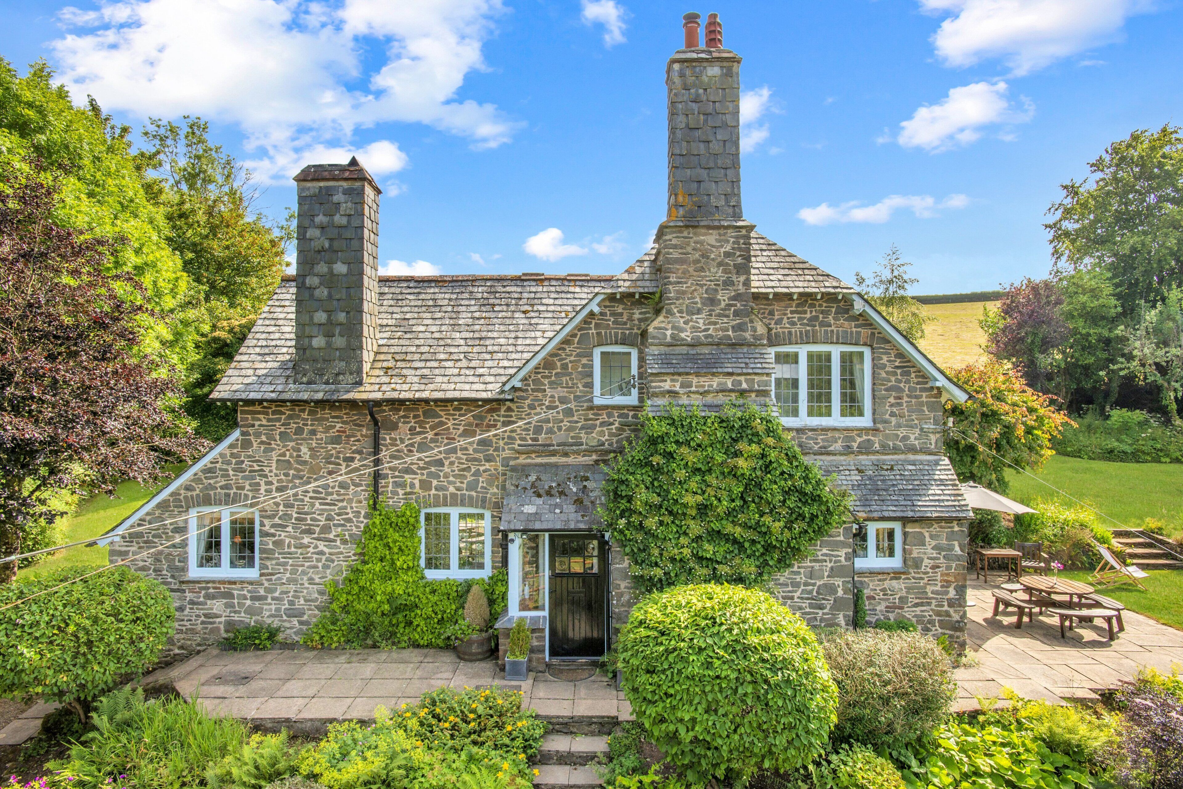 A stone house with a chimney, a front door, and a patio with outdoor furniture.
