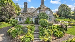 Une maison en pierre avec une cheminée, une porte d’entrée et un jardin avec un sentier en pierre menant à l’entrée.