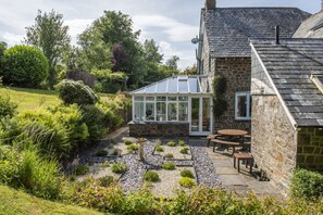 Una casa in pietra con veranda, un giardino con vialetto in ghiaia e un patio con mobili da esterno.