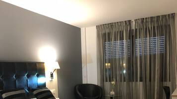 Ein modernes Hotelzimmer mit einem großen Bett, einem Sessel, einem Schreibtisch und Blick auf die beleuchtete Stadt.