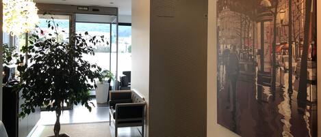A modern hotel lobby with a reception desk, seating area, and a large painting of a cityscape.