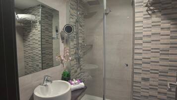 Un baño moderno con cabina de ducha de vidrio, un espejo grande y un lavabo blanco.