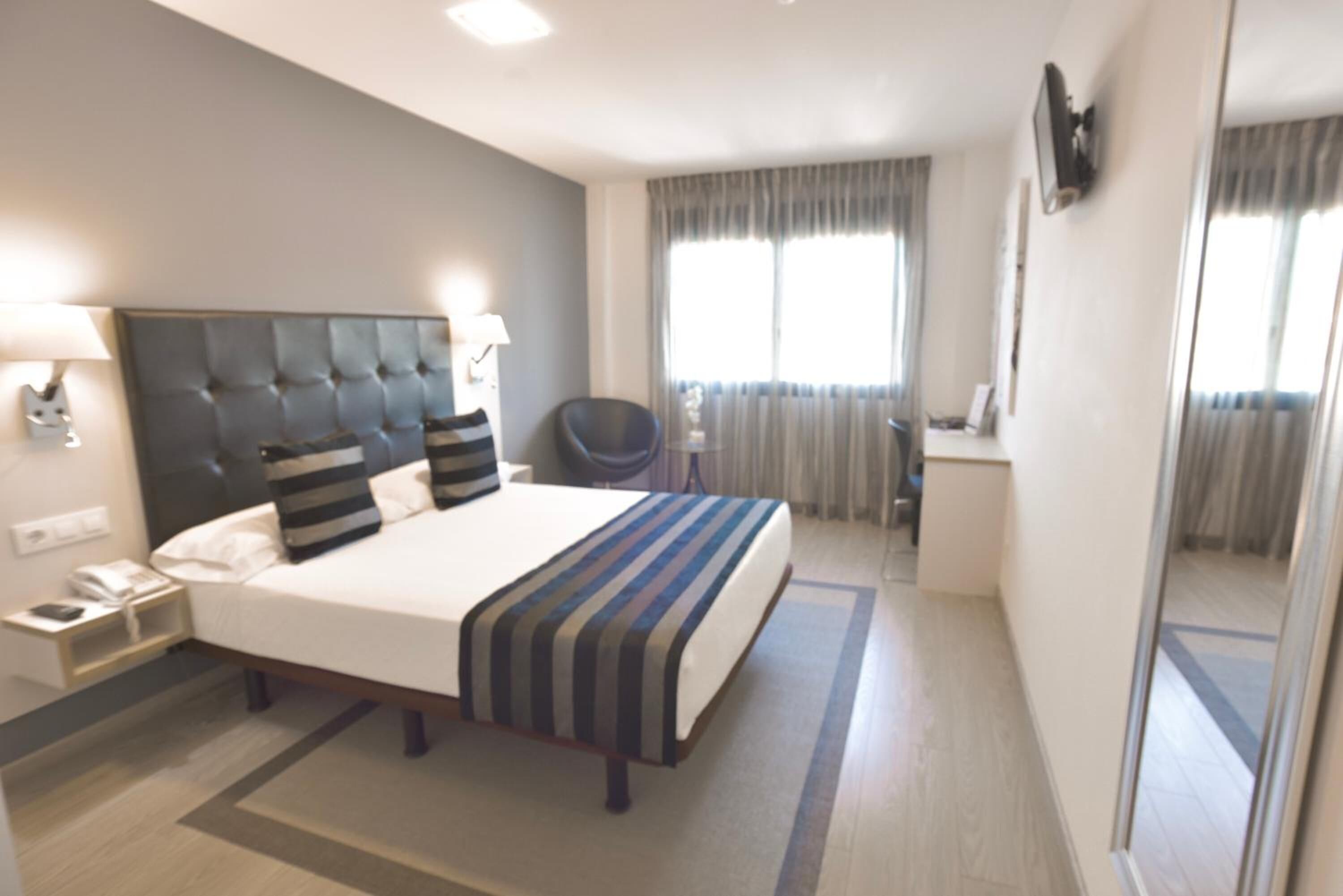 A hotel room with a large bed, bedside tables, a chair, a desk, and a window with curtains.