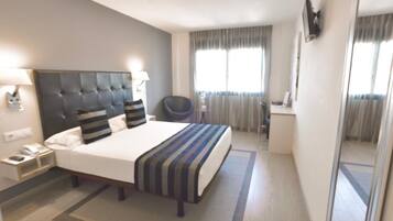 A hotel room with a large bed, bedside tables, a chair, a desk, and a window with curtains.