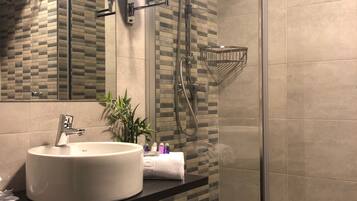 Un baño moderno con un lavabo redondo, un espejo, un cabezal de ducha de mano y una ducha con mampara de vidrio.