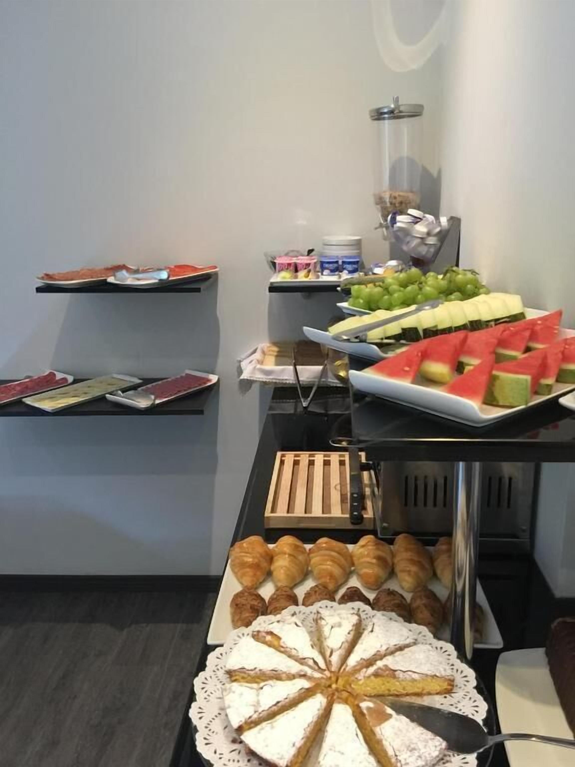 Un bufé con distintos alimentos, incluyendo sandía, uvas y pasteles.