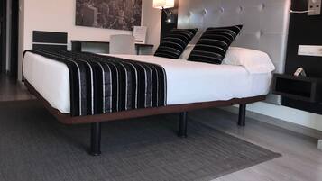 A modern hotel room with a large bed, two bedside tables, a nightstand, a wall-mounted lamp, and a cityscape artwork above the bed.