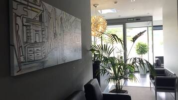 A modern lobby with a large abstract painting, a reception desk, and a seating area with potted plants.