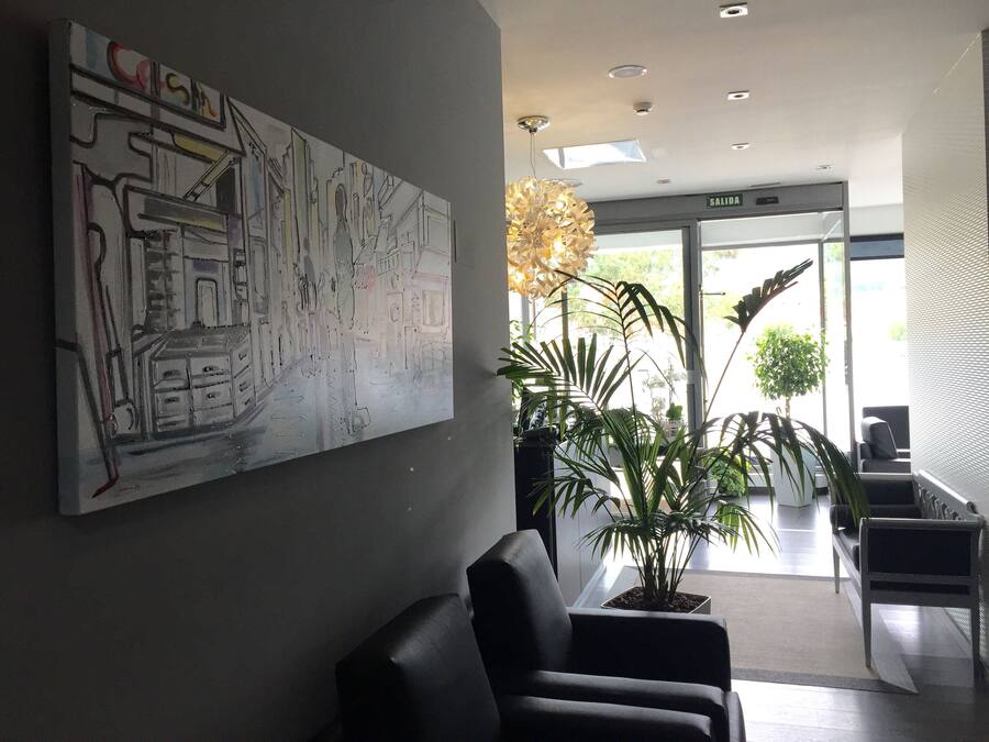 A modern lobby with a large abstract painting, a reception desk, and a seating area with potted plants.