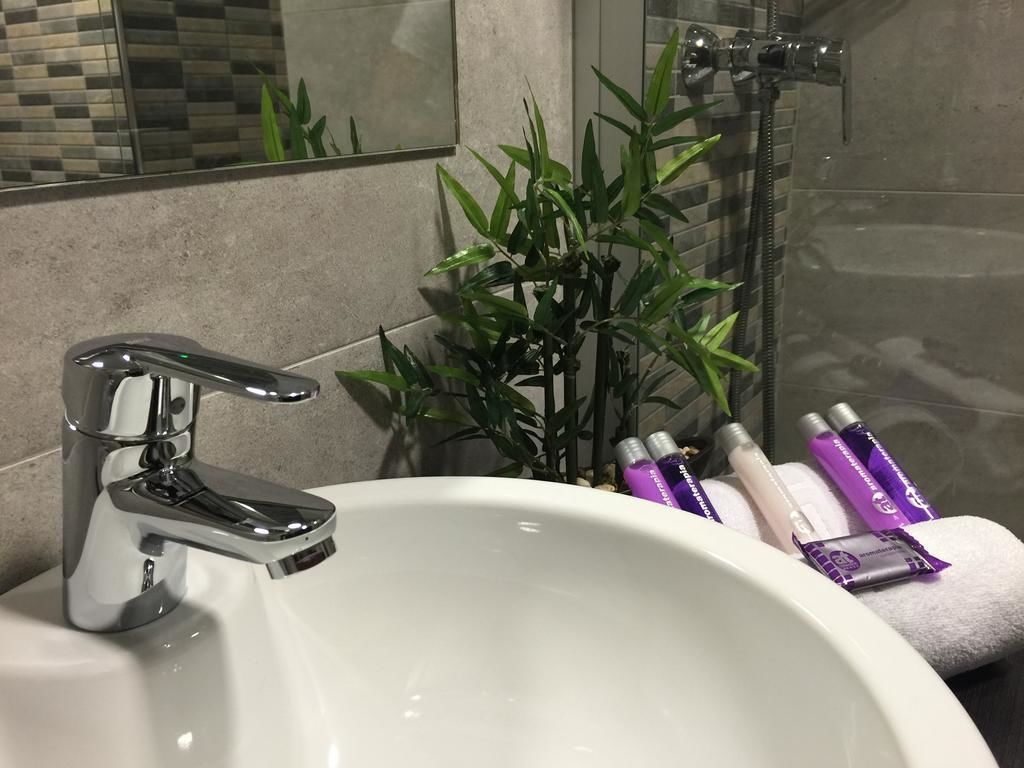 A bathroom with a white sink, chrome faucet, and a bamboo plant. There are toiletries on the edge of the sink.