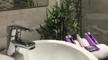 A bathroom with a white sink, chrome faucet, and a bamboo plant. There are toiletries on the edge of the sink.