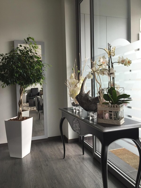 A modern interior with a large potted tree, a glass table with decorative items, and a view through a window. - Hotel Noia (Noia)