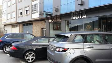 Un edificio de hotel con fachada moderna, dos coches estacionados y el letrero del hotel a la vista.