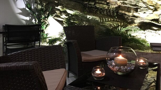 A cozy outdoor seating area with wicker furniture and a table set with candles and decorative stones. - Hotel Noia (Noia)