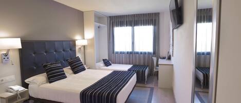 A hotel room with two beds, a desk, a chair, a TV mounted on the wall, and a telephone on the nightstand.