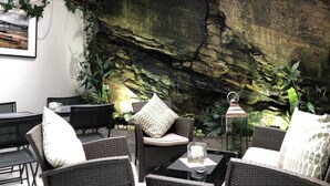 An outdoor seating area with wicker furniture, a table with a candle, and a rock wall backdrop. - Hotel Noia (Noia)
