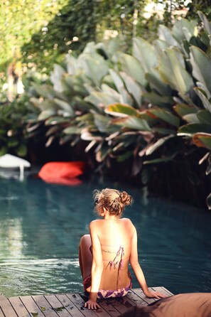 Eine Person sitzt am Pool, im Hintergrund üppiges Grün.