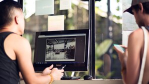 A person using a laptop at a desk with a window view, a keyboard, and a mouse. - M Boutique Hostel (Keroboken Kelod)