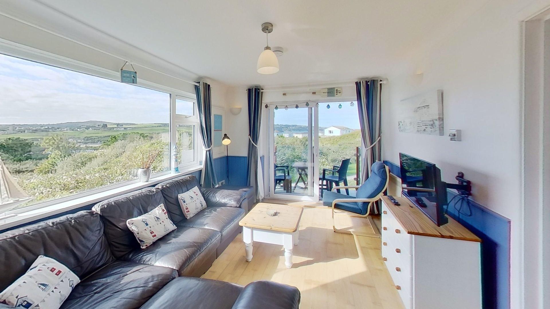 A room with a sofa, a table, a chair, a TV, and a view of the outdoors.