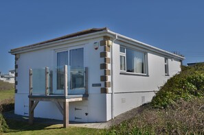 Un piccolo edificio a un piano, di colore bianco, con tetto piatto, ingresso con porta in vetro e un piccolo portico.