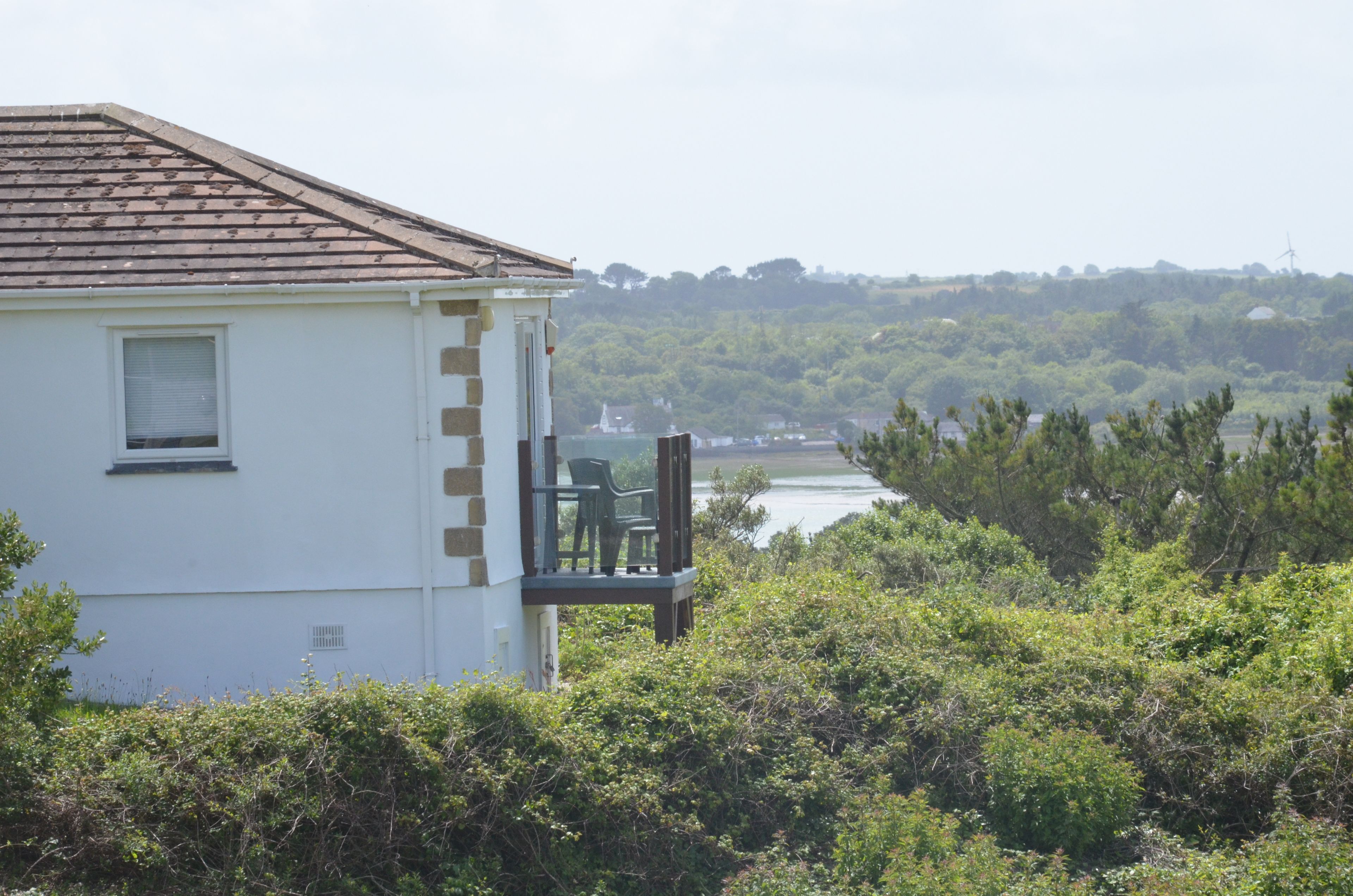 A white building with a balcony overlooking a river and greenery.