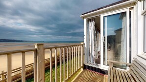 A wooden deck with a glass door leading to a room with a view of the beach and ocean.
