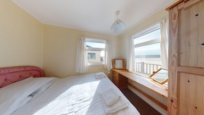 A bedroom with a bed, a wooden dresser, a window with a view of the beach, and a ceiling light.