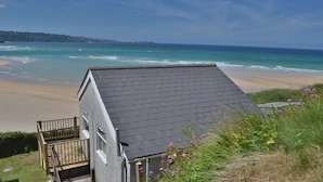 A house with a dark roof, a wooden deck, and a view of the beach and ocean.
