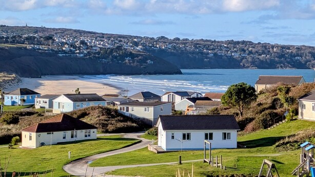 A coastal residential area with houses, a beach, and a hill in the background.