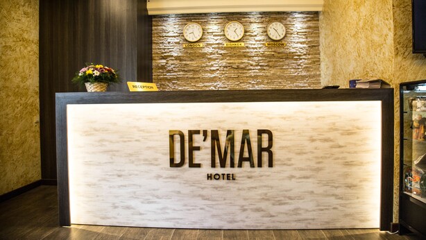 A reception desk with a marble top, clocks displaying times for London, Bishkek, and Moscow, and a reception sign. - De'Mar Hotel (Bishkek)