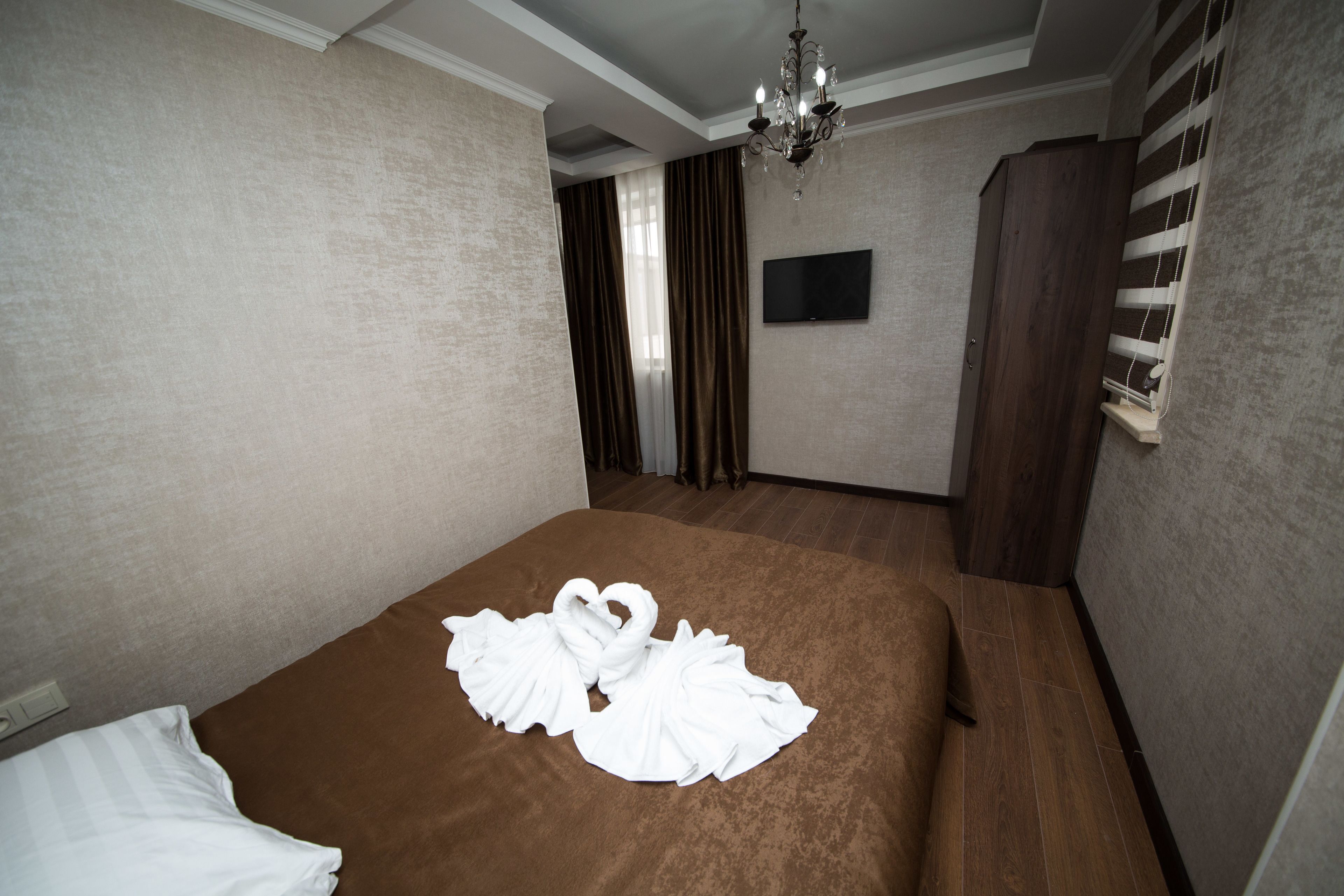 A hotel room with a large bed, a flat-screen TV, a chandelier, and a window with curtains.