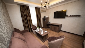 A modern living room with a brown sofa, a round chair, a coffee table, and a TV mounted on the wall. - De'Mar Hotel (Bishkek)