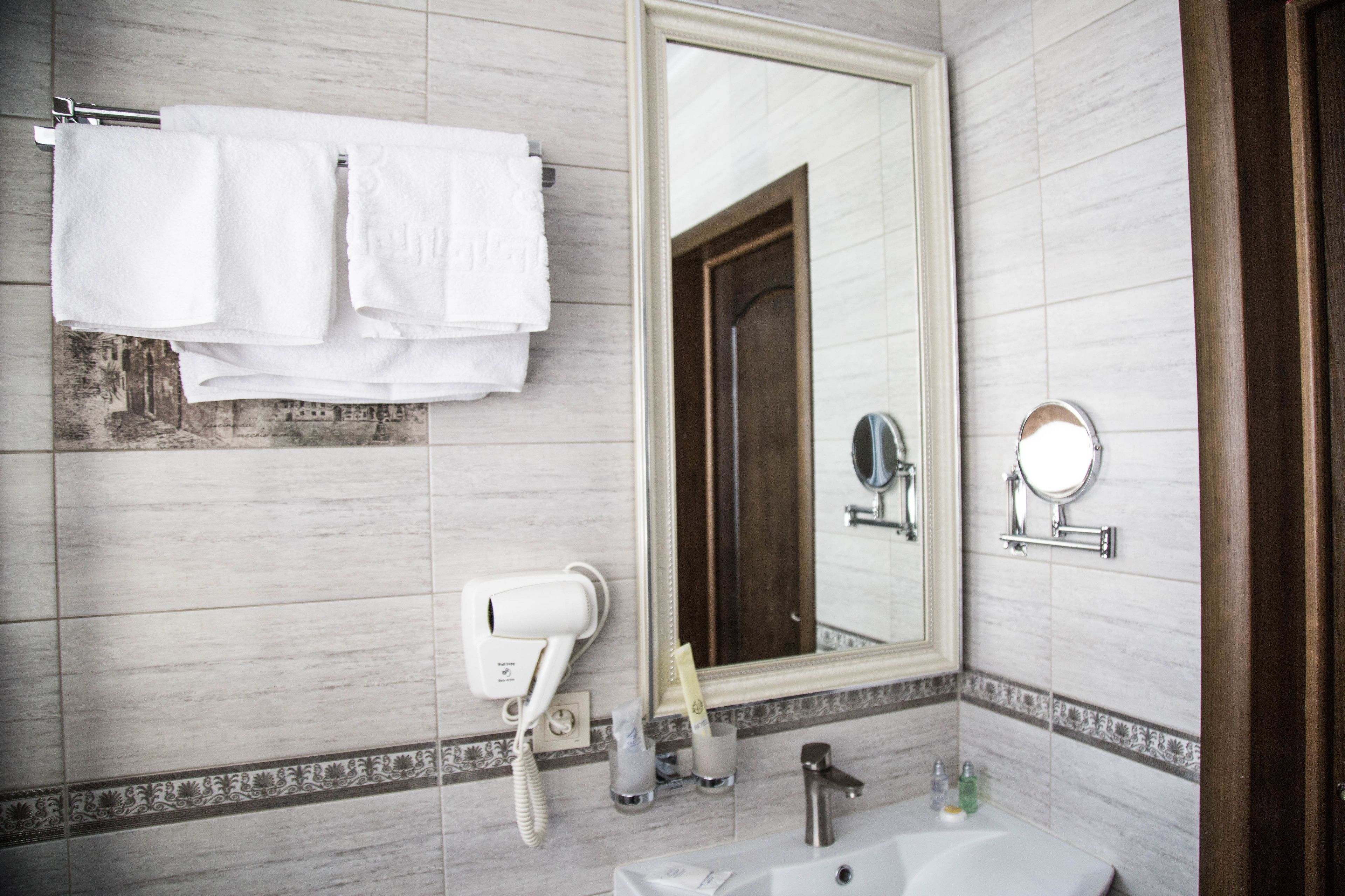 A bathroom with a large mirror, a sink, a towel rack with two towels, a hairdryer, and toiletries.