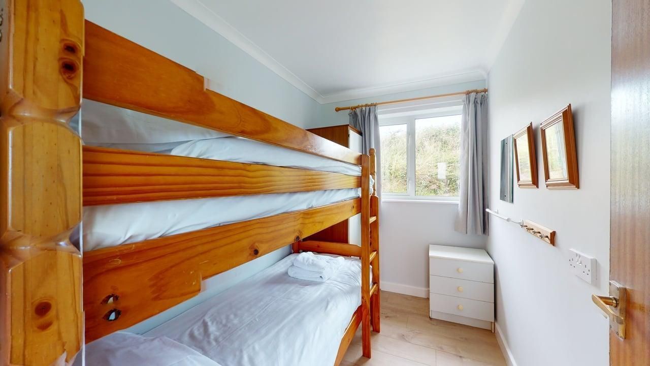 A bunk bed room with a window, a bedside table, and a wall-mounted shelf.