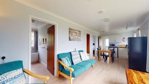 Ein gemütliches Wohnzimmer mit einem blaustürkis-farbenen Sofa, einem Holztisch und einer Küchenzeile mit Schränken und Geräten.