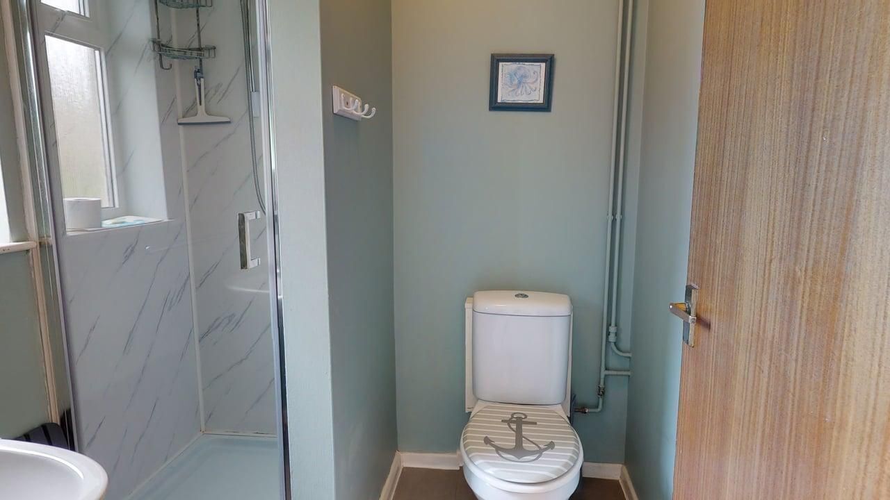 Een badkamer met toilet, douche en een klein raam.